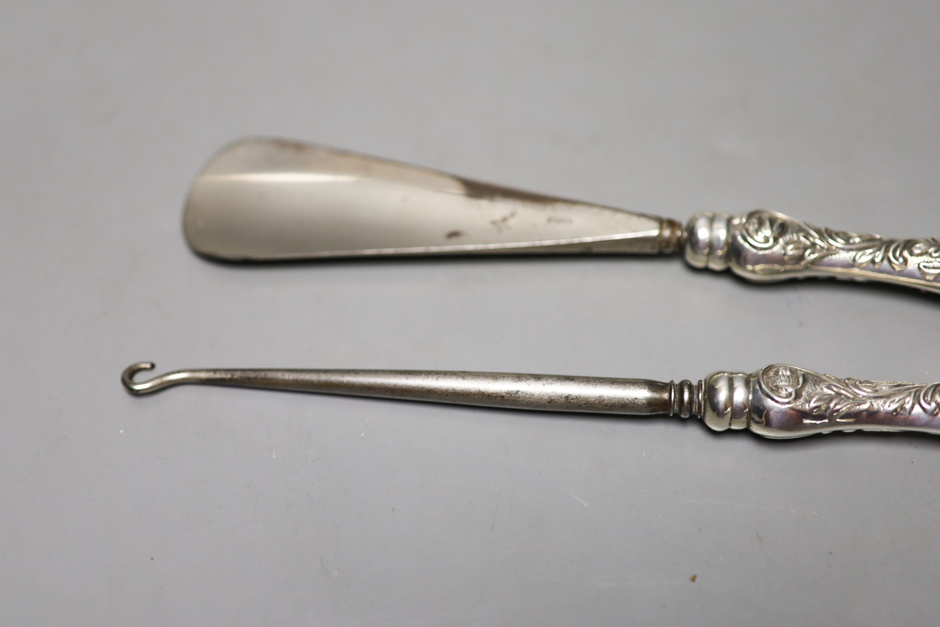 A late Victorian repousse silver mounted hand mirror, London, 1899, two silver mounted glass toilet jars, a silver handled button hook, silver handled shoe horn and a clothes brush.